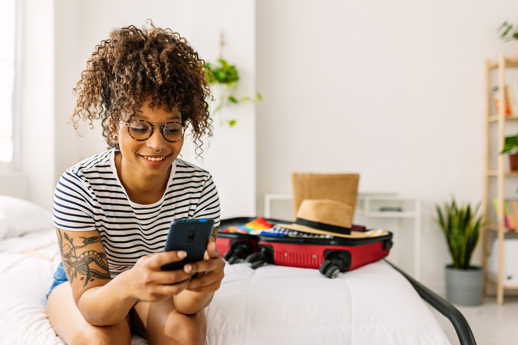 Una giovane donna afroamericana felice prenota una camera d'albergo mentre prepara la sua borsa per le vacanze estive