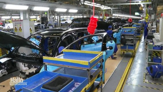 Veduta stradale di una fabbrica di automobili: diversi dipendenti lavorano su modelli di automobili non finiti.  ©schermata 