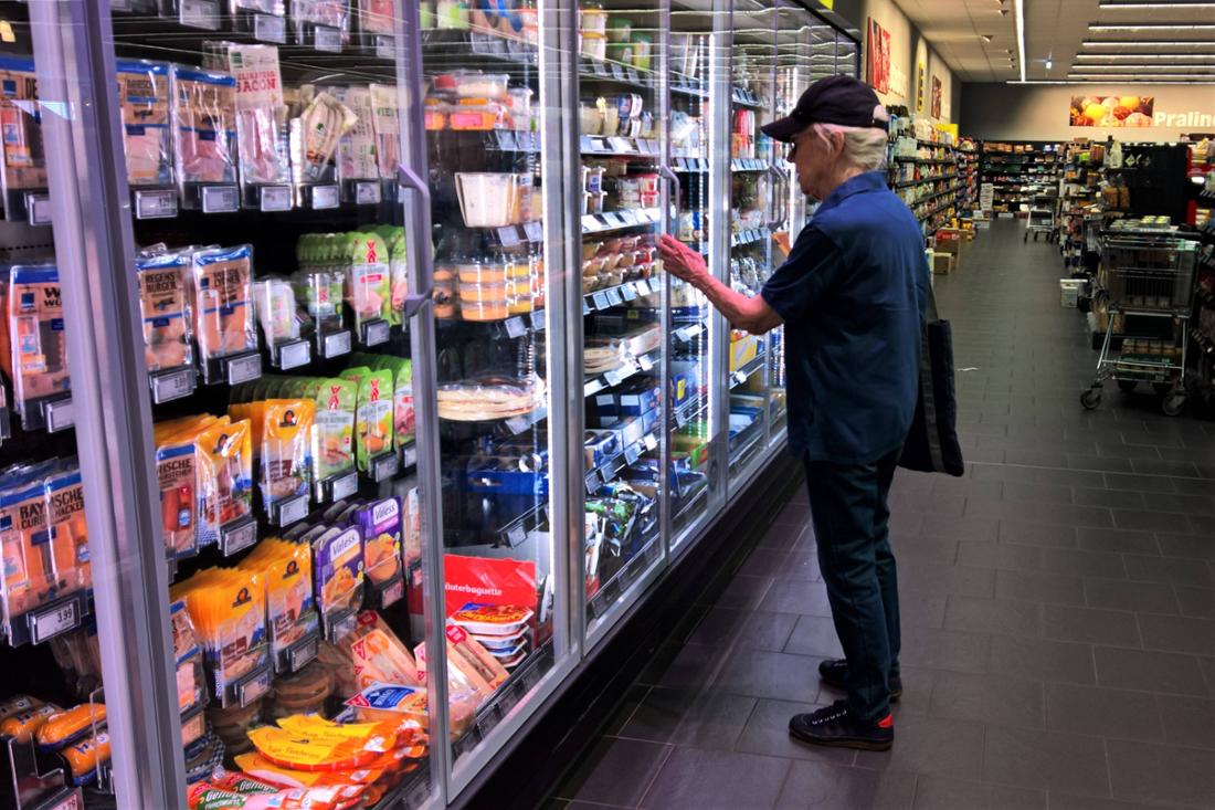 Un cliente Edeka si trova davanti al bancone refrigerato del supermercato contenente pesce, carne, salsicce e creme spalmabili.